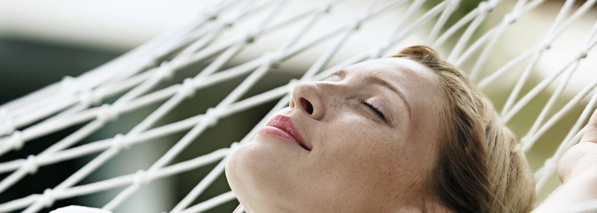 Eine junge Frau entspannt mit Kopfhörern in einer weissen Netz-Hängematte.